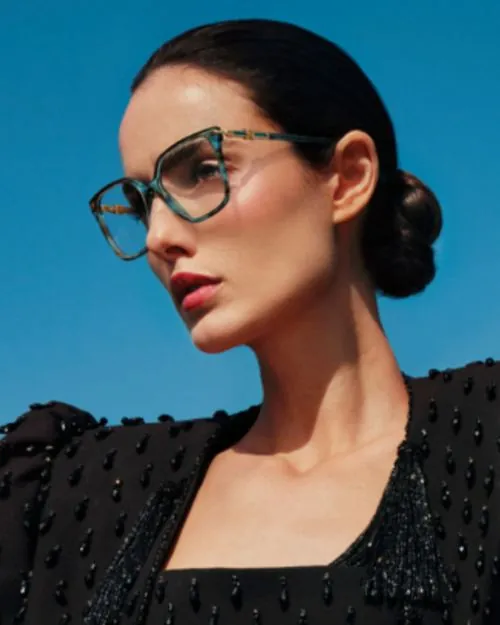 Mujer con aros oftálmicos Carolina Herrera de acetato azul y dorado, disponibles en Ópticas CV+