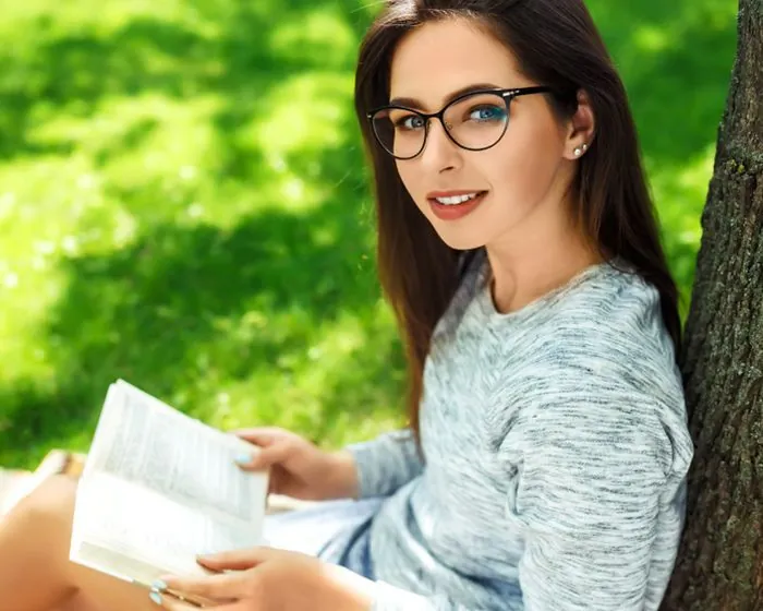 Mujer con lentes de visión sencilla leyendo cómodamente al aire libre, disponibles en Ópticas CV+